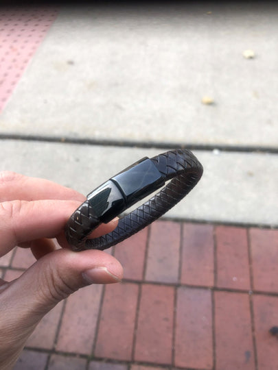 Black woven bracelet held by a hand on a pavement background