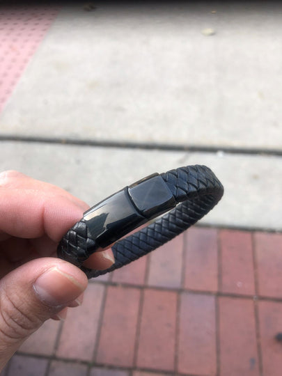 Black braided bracelet held by a hand on a pavement background