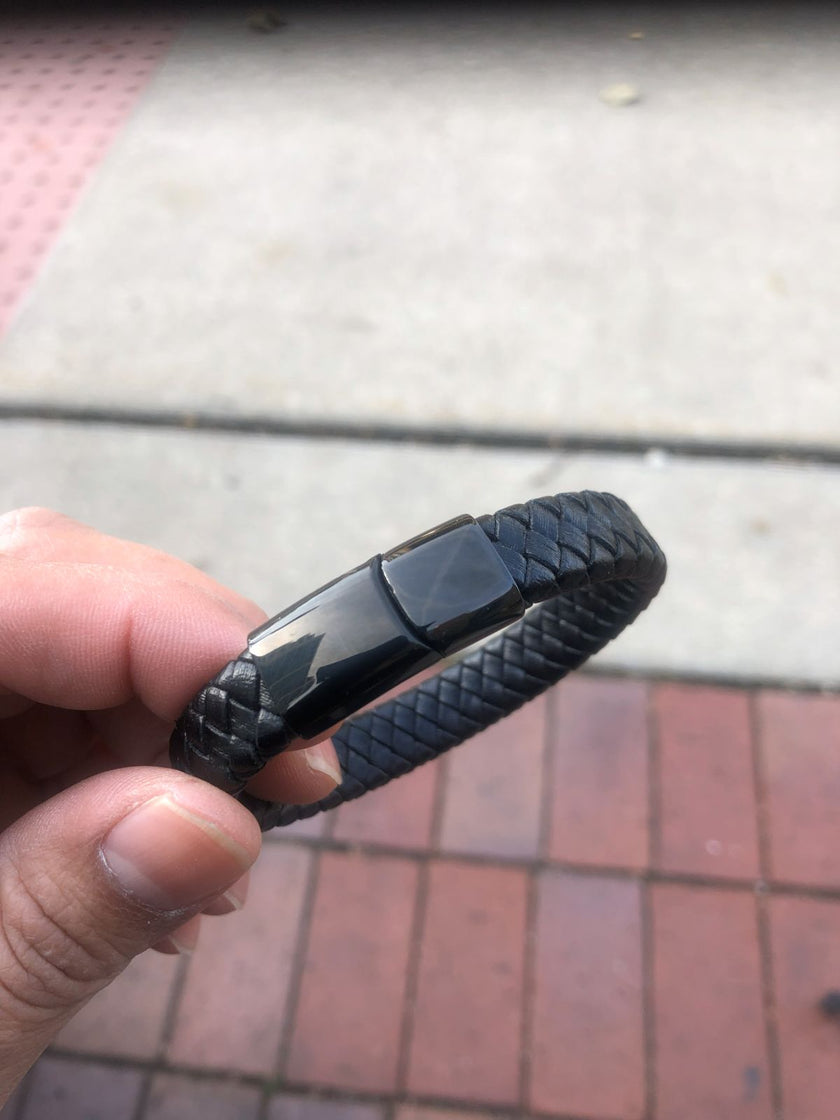 Black braided bracelet held by a hand on a pavement background