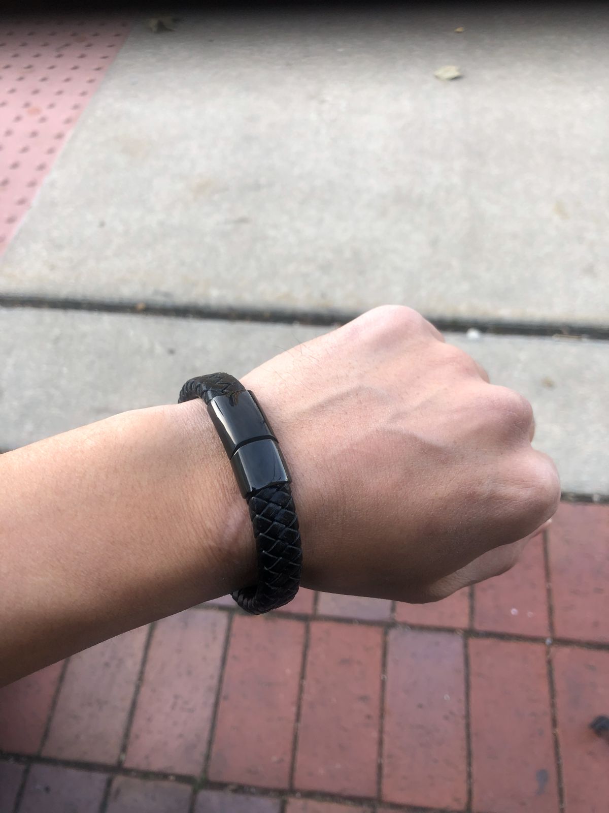 Person wearing a black smartwatch on a wrist with a sidewalk background