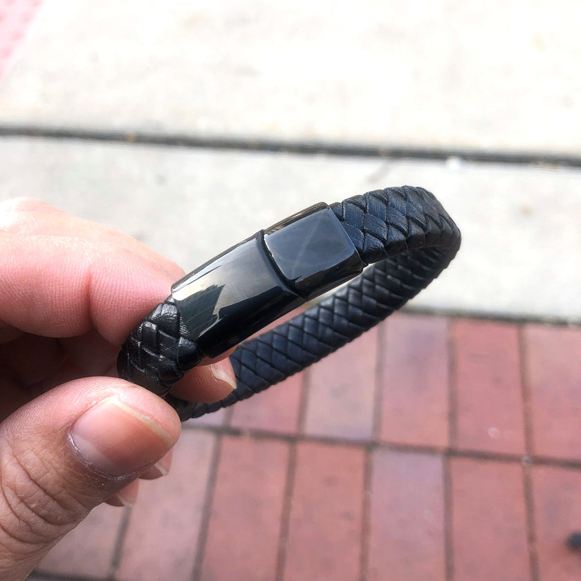 Black braided bracelet held by a hand on a blurred outdoor background