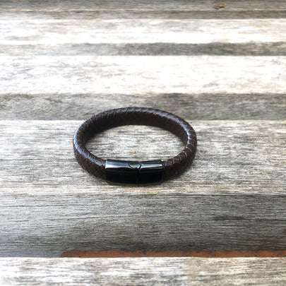 Brown leather bracelet with a black clasp on a wooden surface