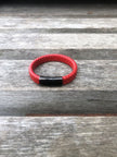 Red braided bracelet with a black clasp on a wooden surface
