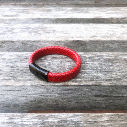 Red braided bracelet with a black clasp on a wooden surface