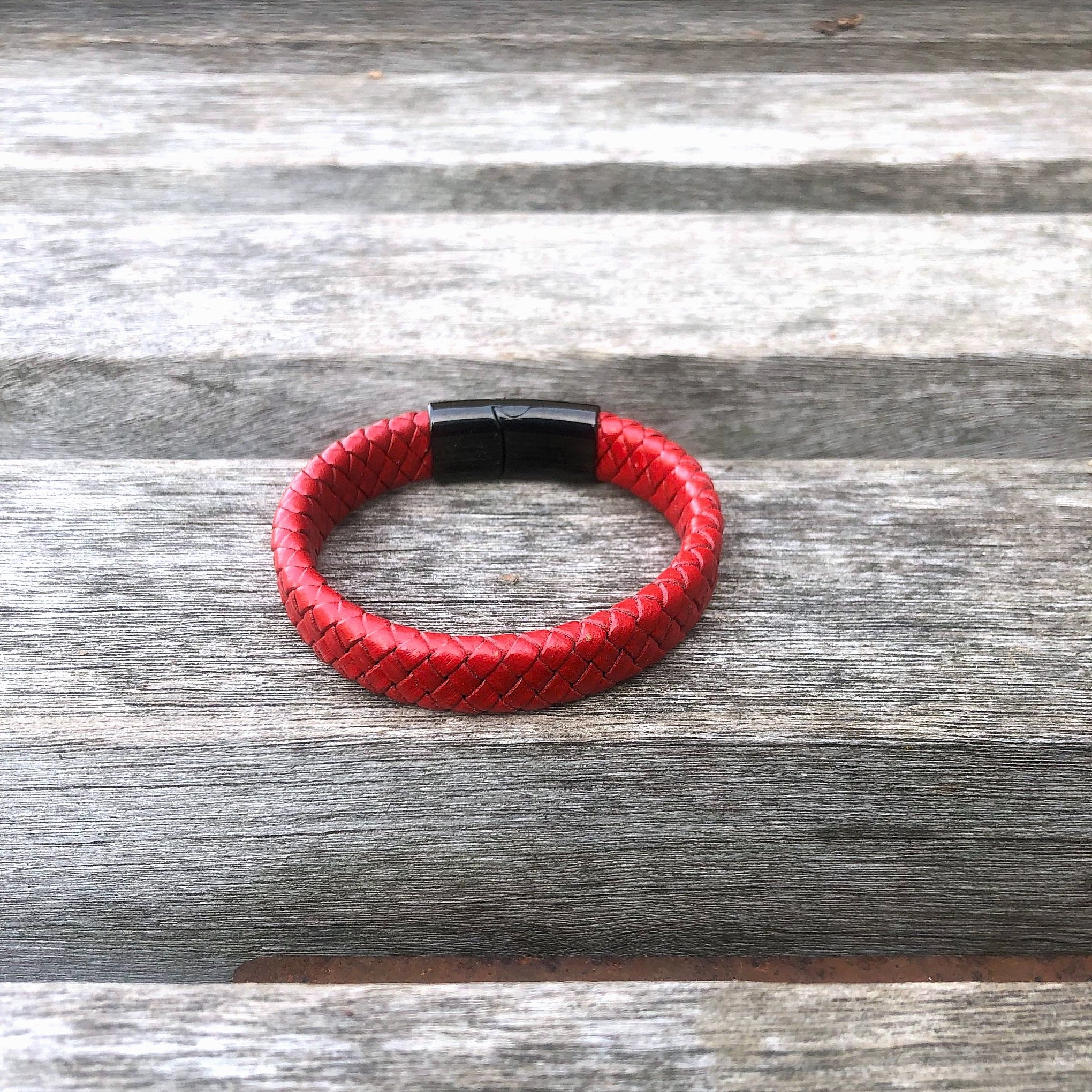 Red braided leather bracelet with black clasp on a wooden surface
