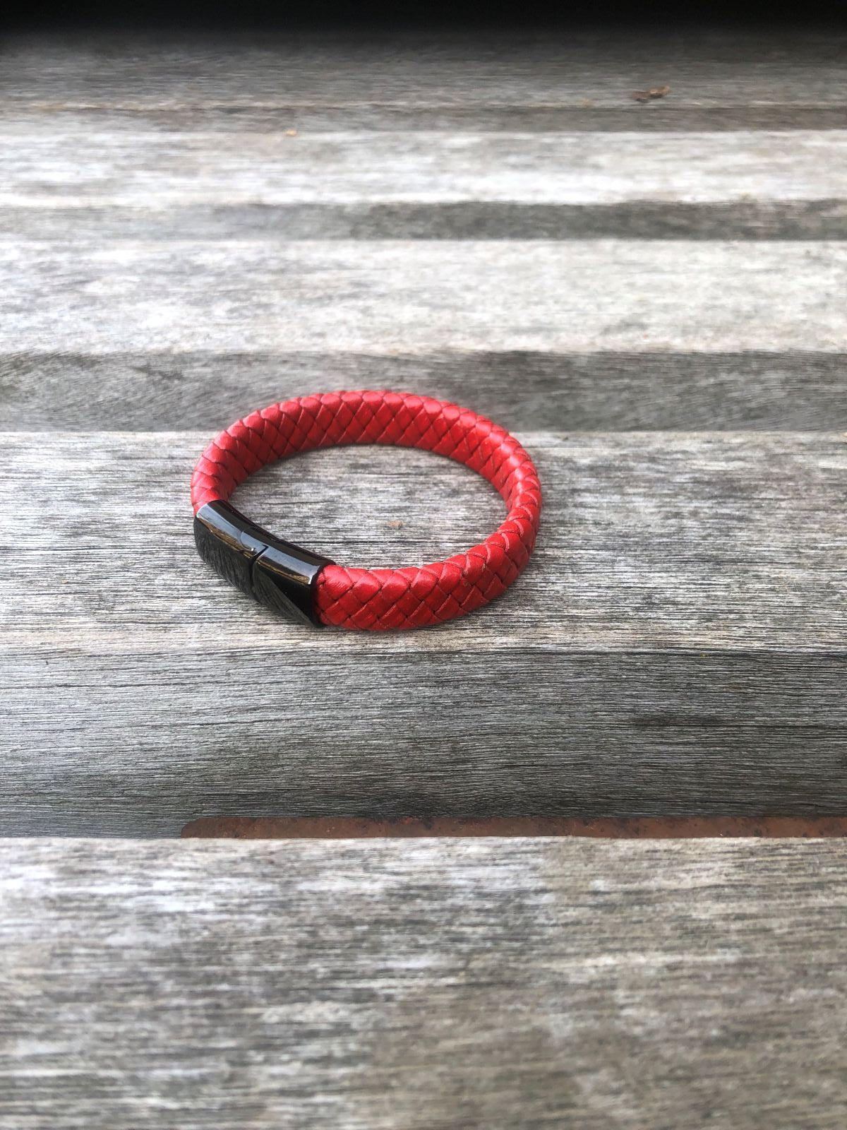 Red braided leather bracelet with black clasp on a wooden surface