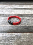 Red braided leather bracelet with black clasp on a wooden surface