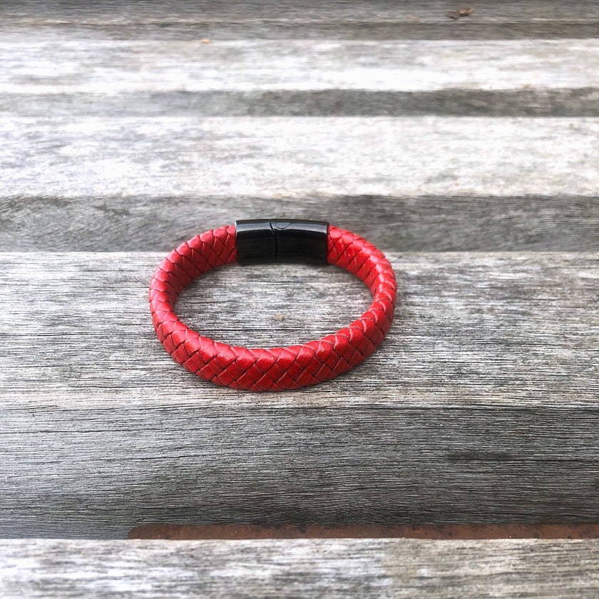 Red braided leather bracelet with black clasp on a wooden surface