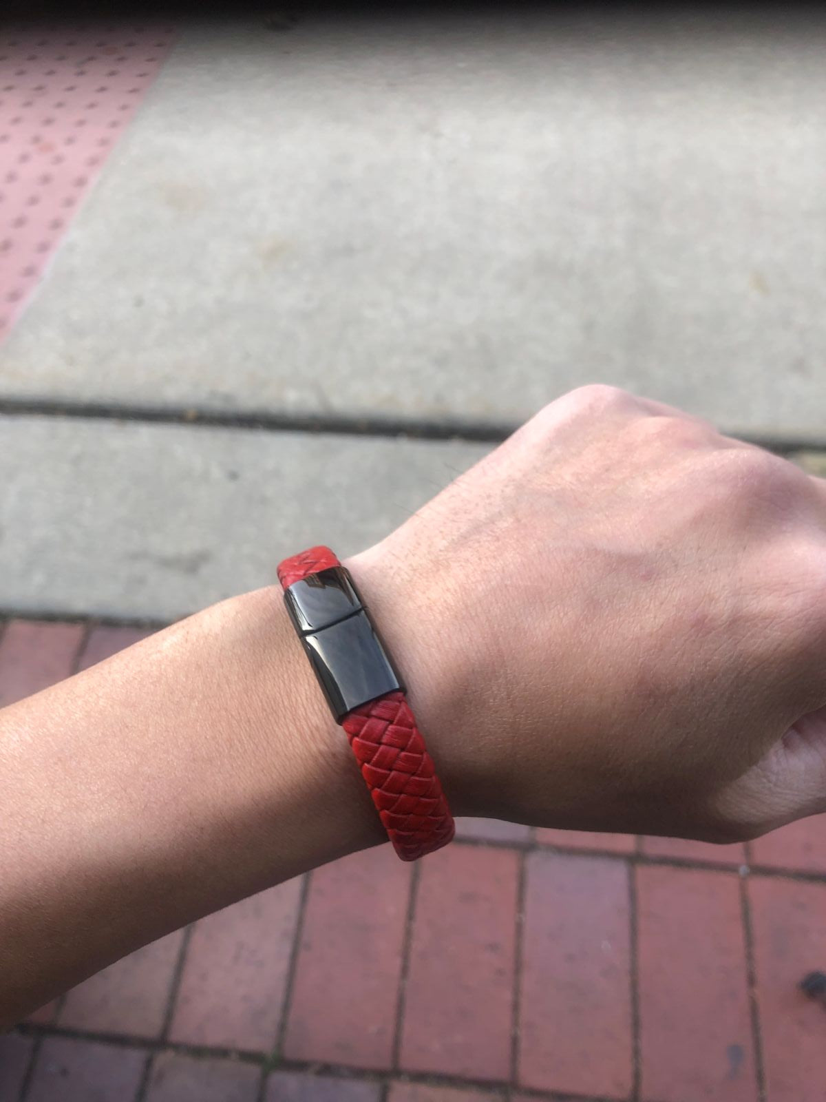 Red bracelet with a metallic clasp on a wrist, against a pavement background
