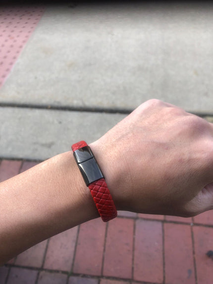 Red bracelet with a metallic clasp on a wrist, against a pavement background
