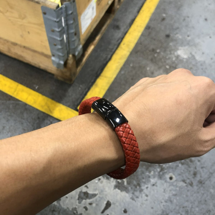 Person wearing a red braided bracelet with a black clasp over a concrete floor.