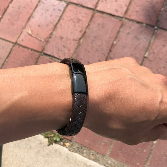 Person wearing a black woven bracelet on a brick pavement background