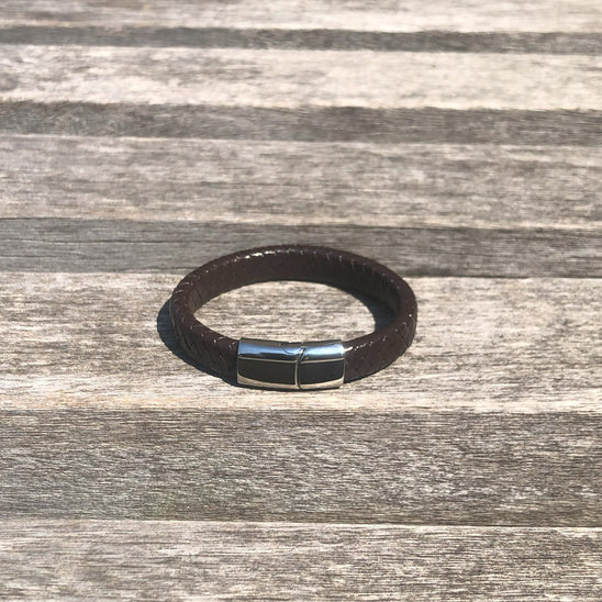 Brown leather bracelet with a silver clasp on a wooden surface