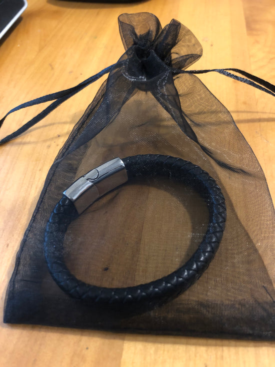 Black braided leather bracelet with a silver clasp on a sheer black fabric background.