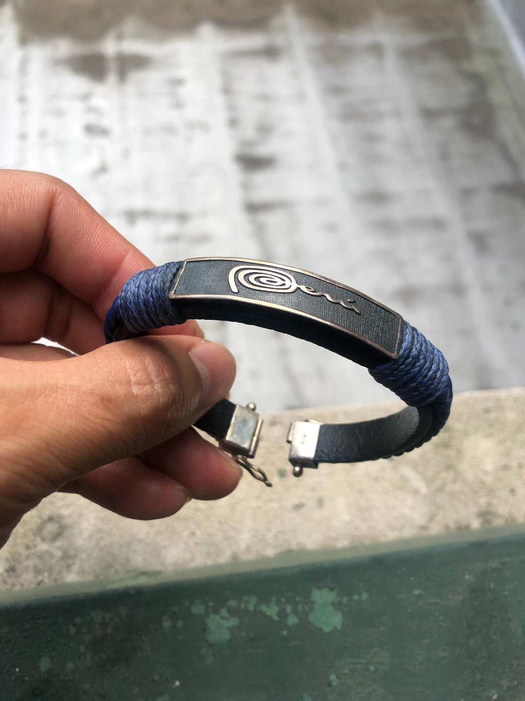 Hand holding a blue bracelet with a metallic clasp against a blurred background