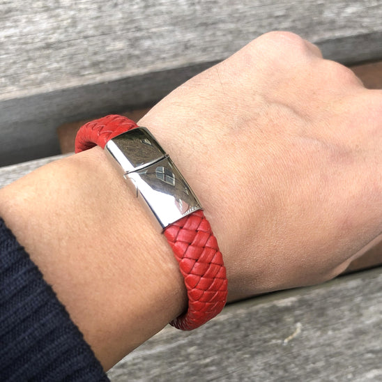 Red braided bracelet on a wrist with a metallic clasp against a wooden background