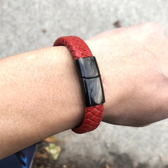 Red braided leather bracelet with a black magnetic clasp on a wrist against a blurred background