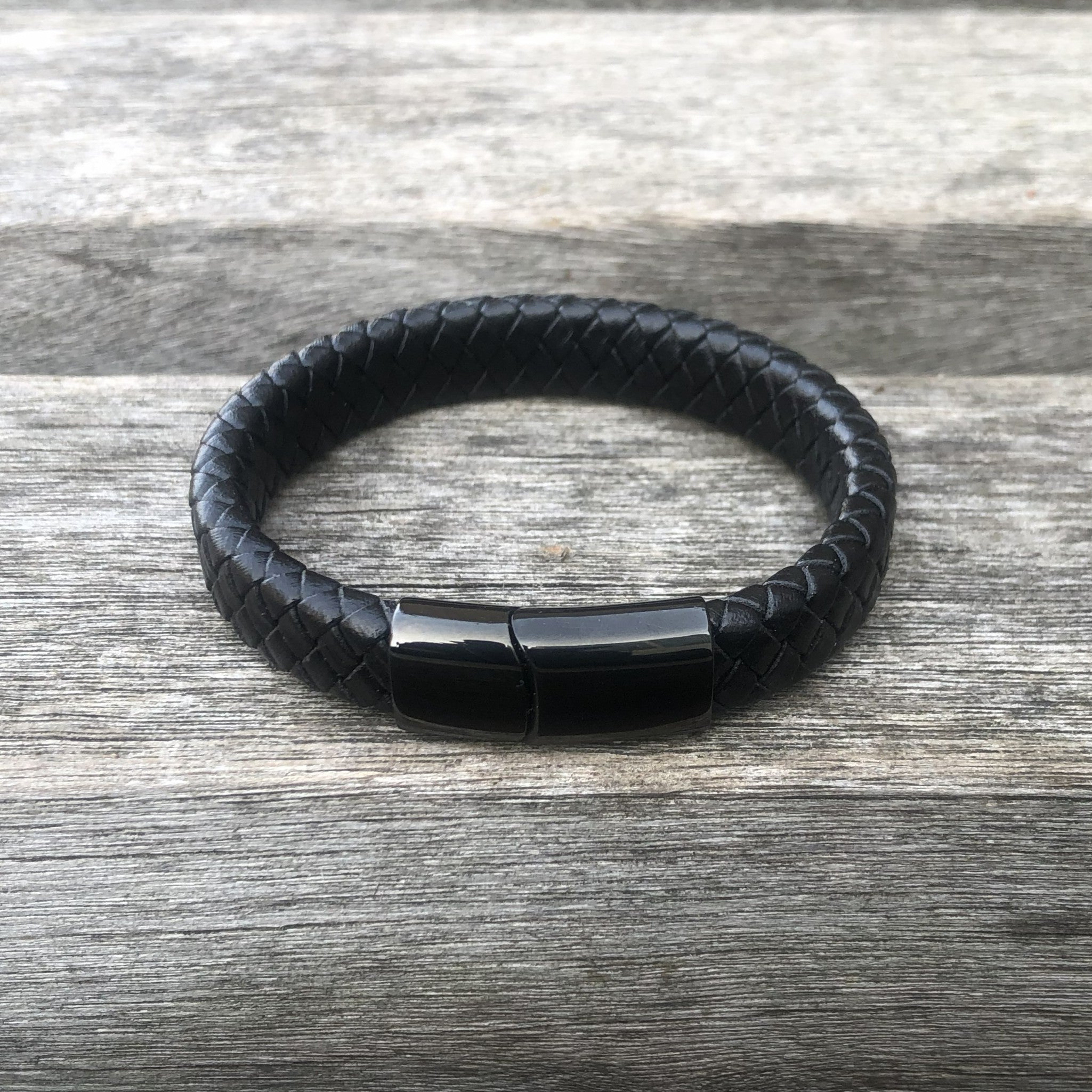 Black braided leather bracelet with a black magnetic clasp on a wooden surface