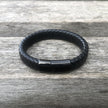 Black braided leather bracelet with a black magnetic clasp on a wooden surface