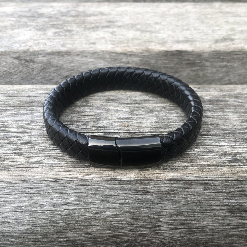 Black braided leather bracelet with a black magnetic clasp on a wooden surface
