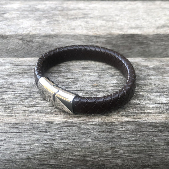 Black leather bracelet with a silver clasp on a wooden surface