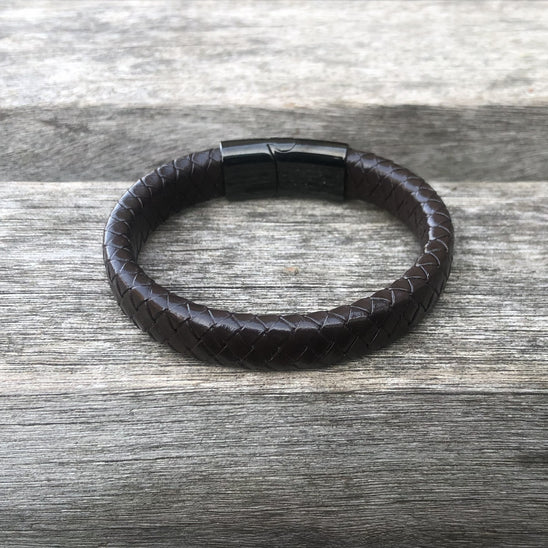 Brown leather bracelet with a black clasp on a wooden surface