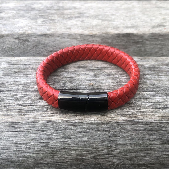 Red braided leather bracelet with a black magnetic clasp on a gray wooden surface