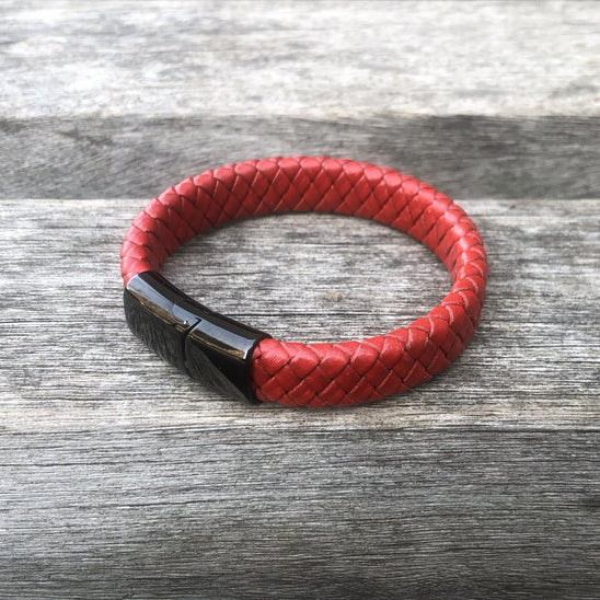 Red braided leather bracelet with a black clasp on a wooden surface