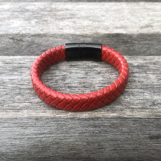 Red braided leather bracelet with a black magnetic clasp on a wooden surface