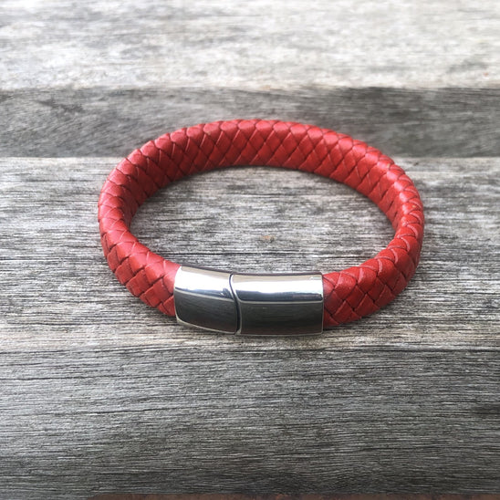 Red braided leather bracelet with a silver clasp on a wooden surface