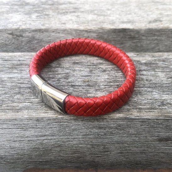 Red braided leather bracelet with a silver clasp on a wooden surface