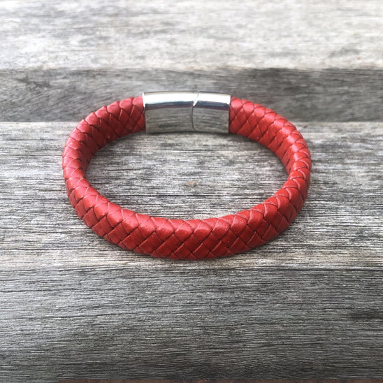 Red braided leather bracelet with silver clasp on a wooden surface