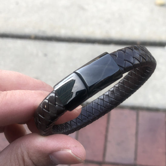 Black woven bracelet held by a hand on a blurred pavement background