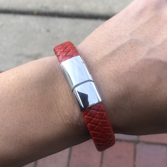 Red braided bracelet with silver clasp on a wrist, blurred background