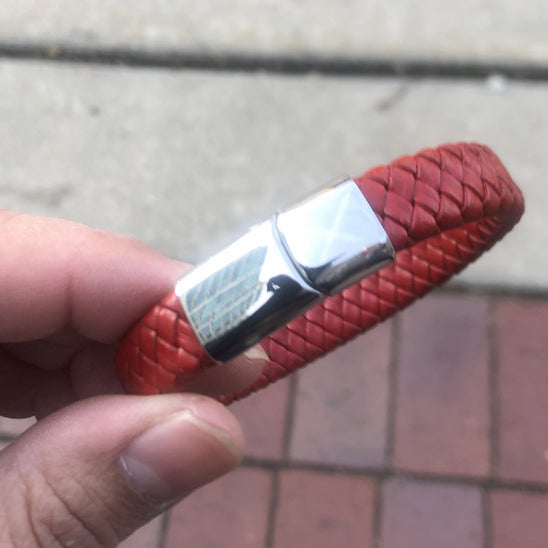 Red braided bracelet with a silver clasp held by a hand on a blurred pavement background