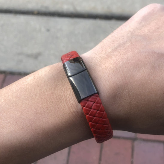 Red woven bracelet with a black clasp on a wrist, blurred background