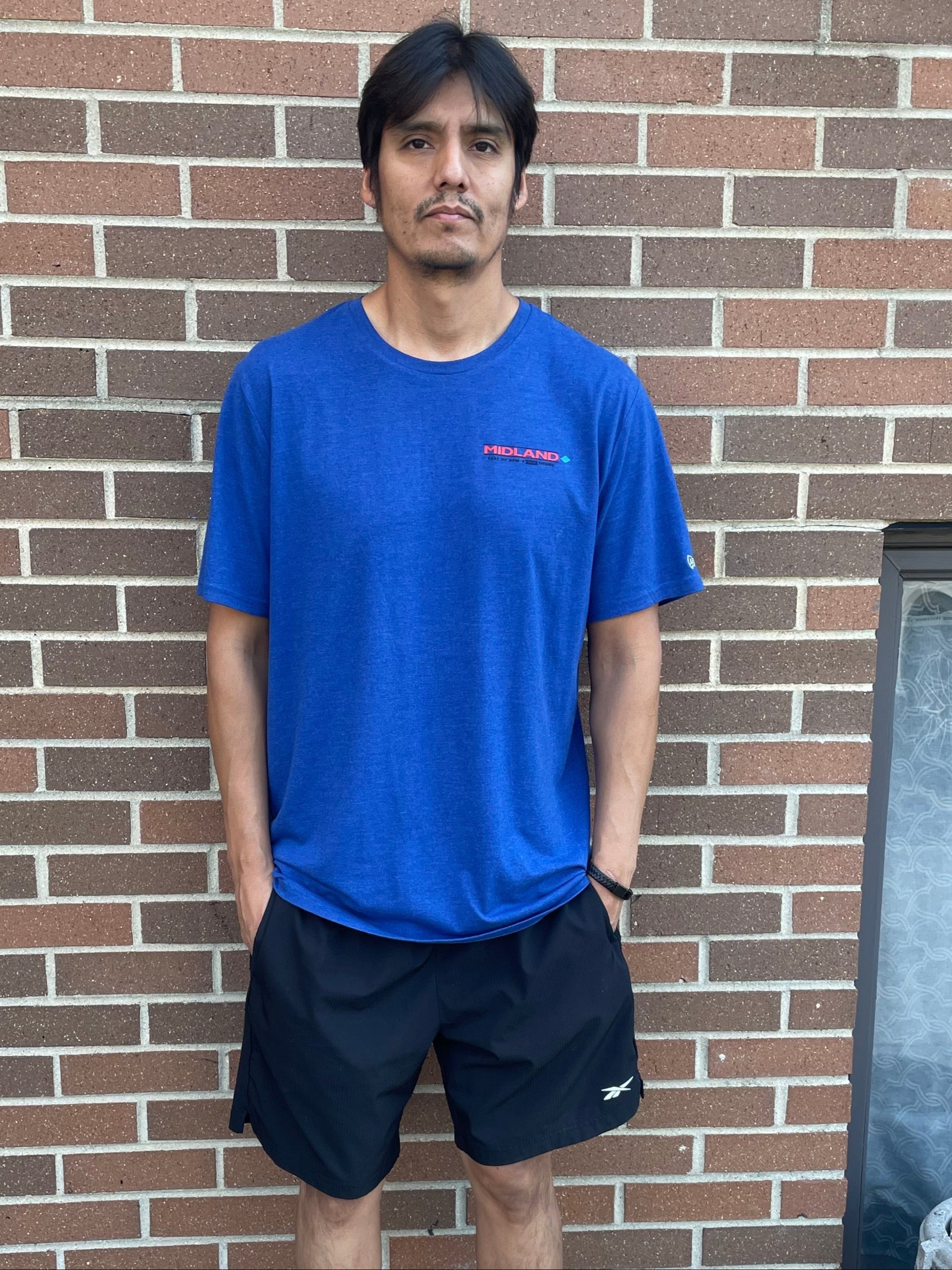 Man in blue shirt and black shorts standing on a brick pavement