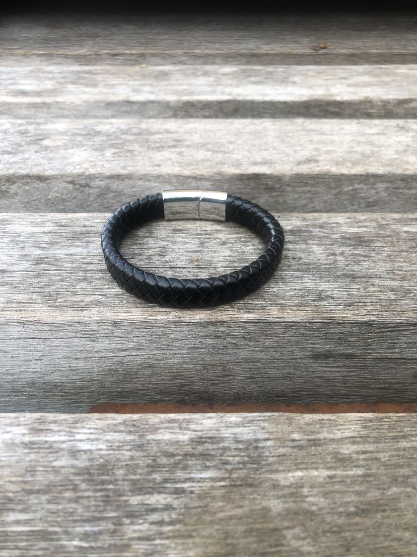 Black leather bracelet with a silver clasp on a wooden surface