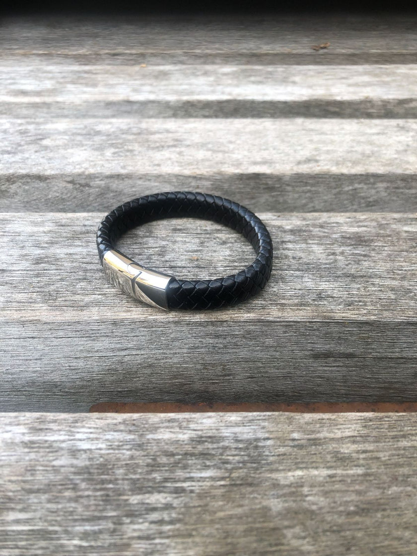 Black leather bracelet with silver clasp on a wooden surface