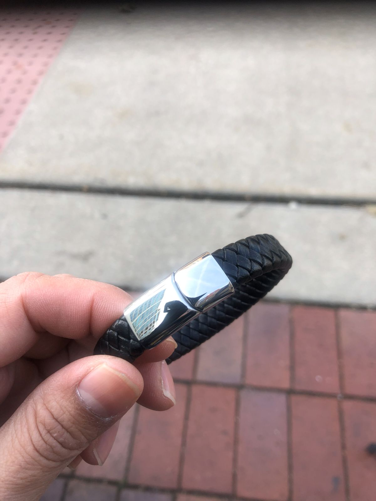 Black leather bracelet with a silver clasp held by a hand on a pavement background
