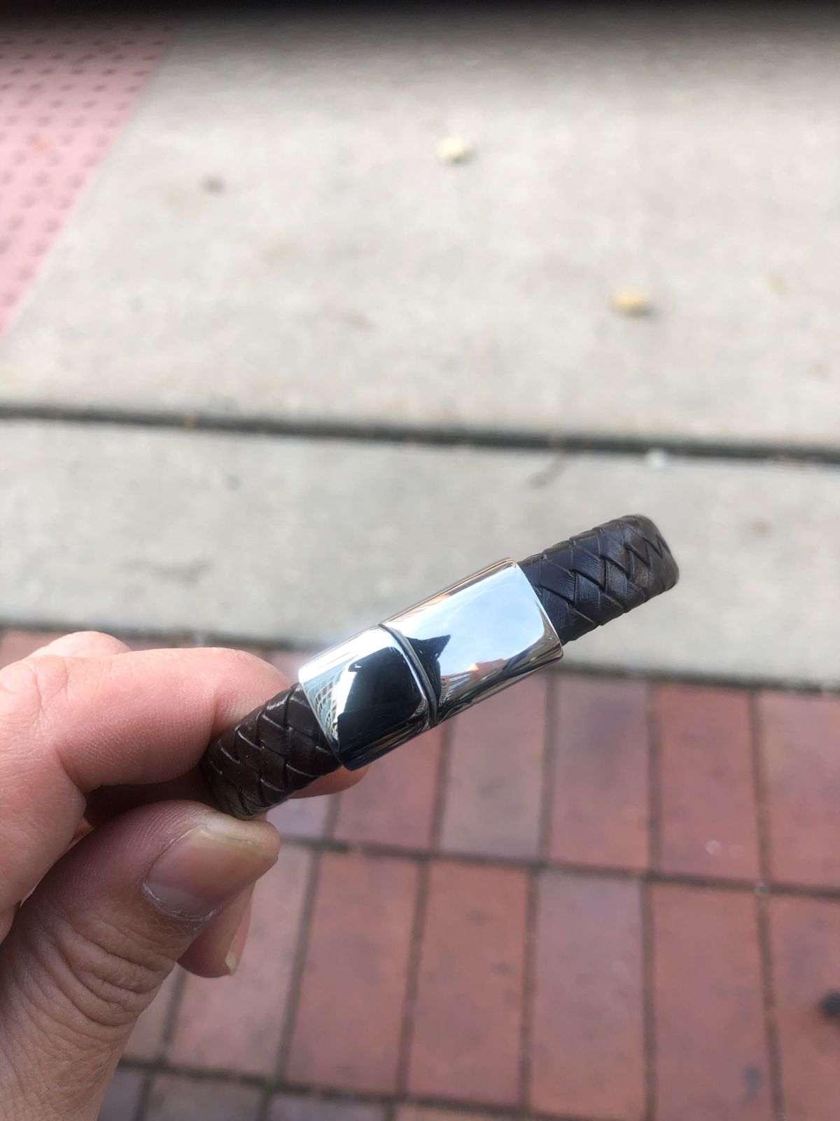 Hand holding a black and silver bracelet on a pavement background
