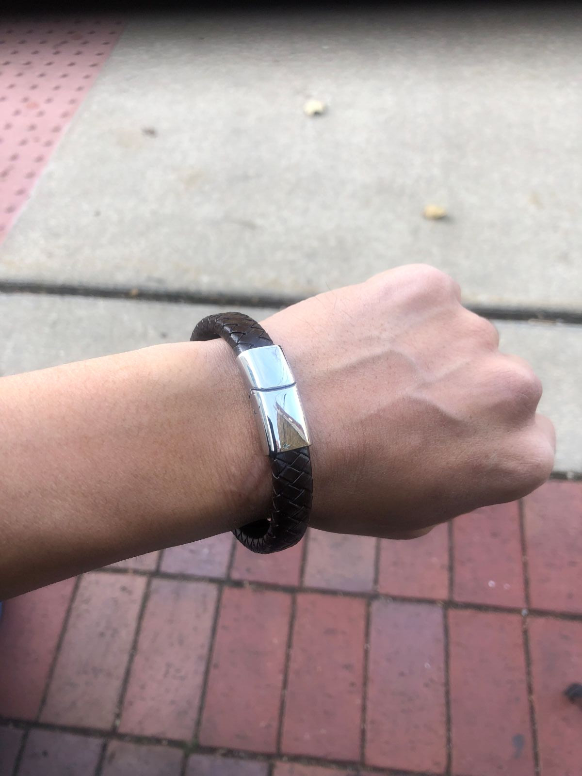 Hand wearing a silver bracelet on a pavement background