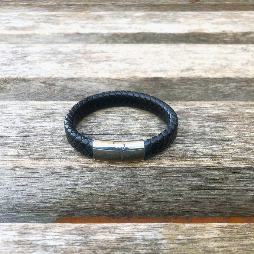 Black leather bracelet with a silver clasp on a wooden surface