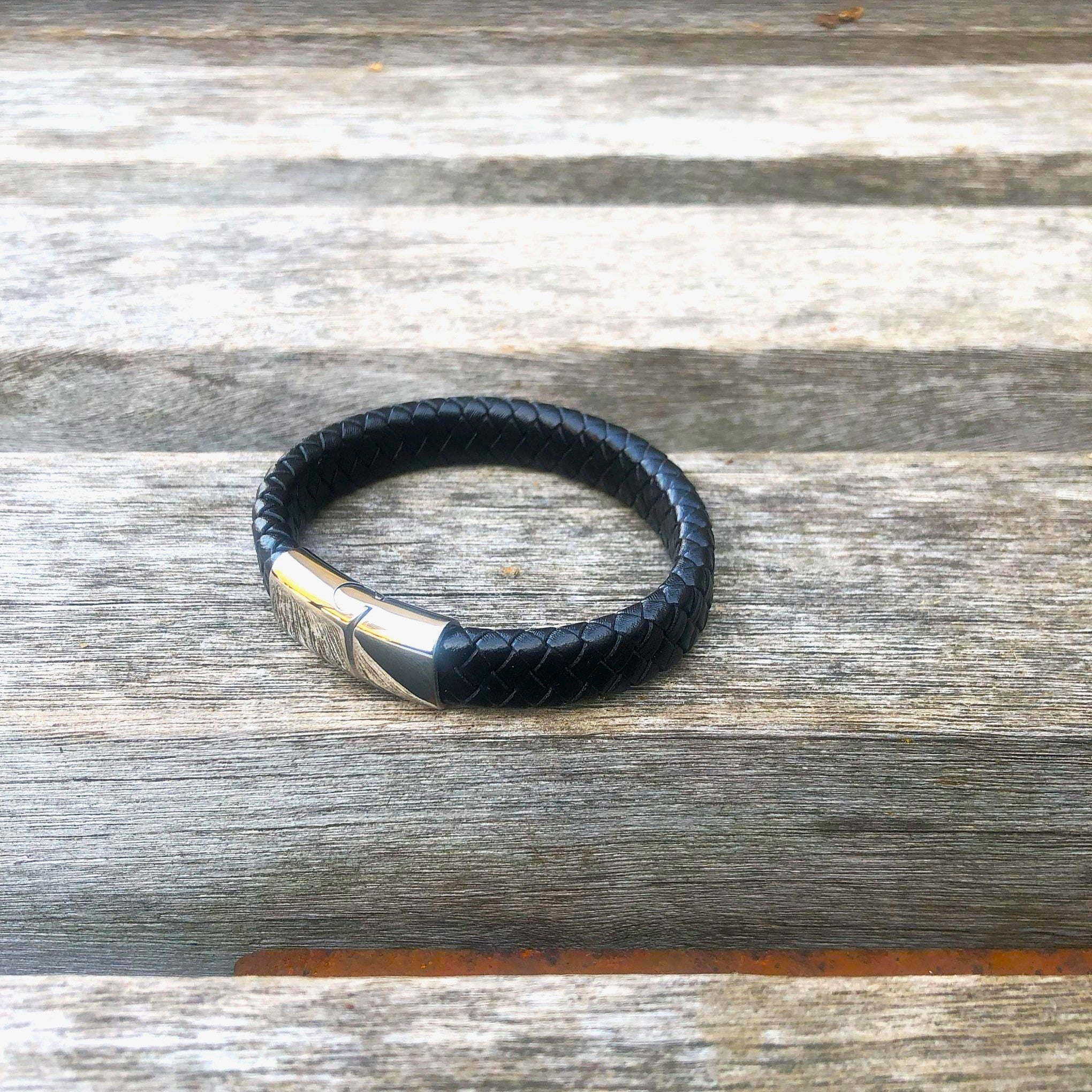 Black leather bracelet with silver clasp on a wooden surface