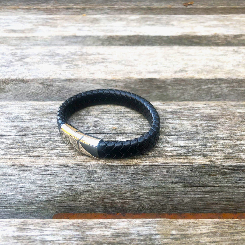 Black leather bracelet with silver clasp on a wooden surface