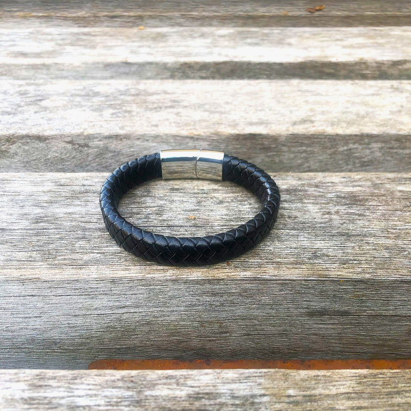 Black leather bracelet with silver clasp on a wooden surface
