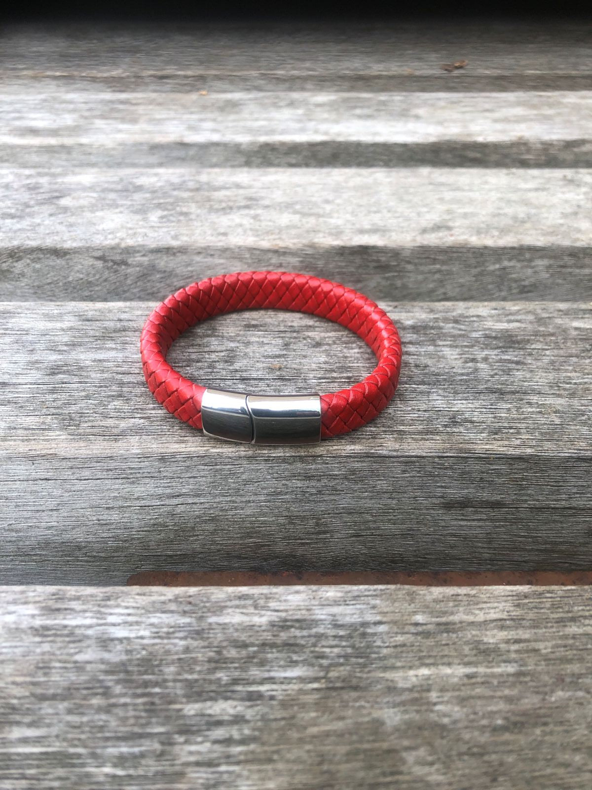 Red leather bracelet with a silver clasp on a wooden surface