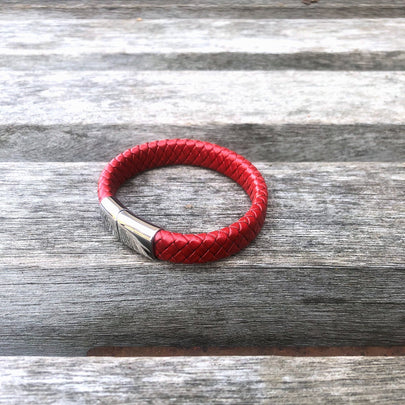 Red braided leather bracelet with a silver clasp on a wooden surface