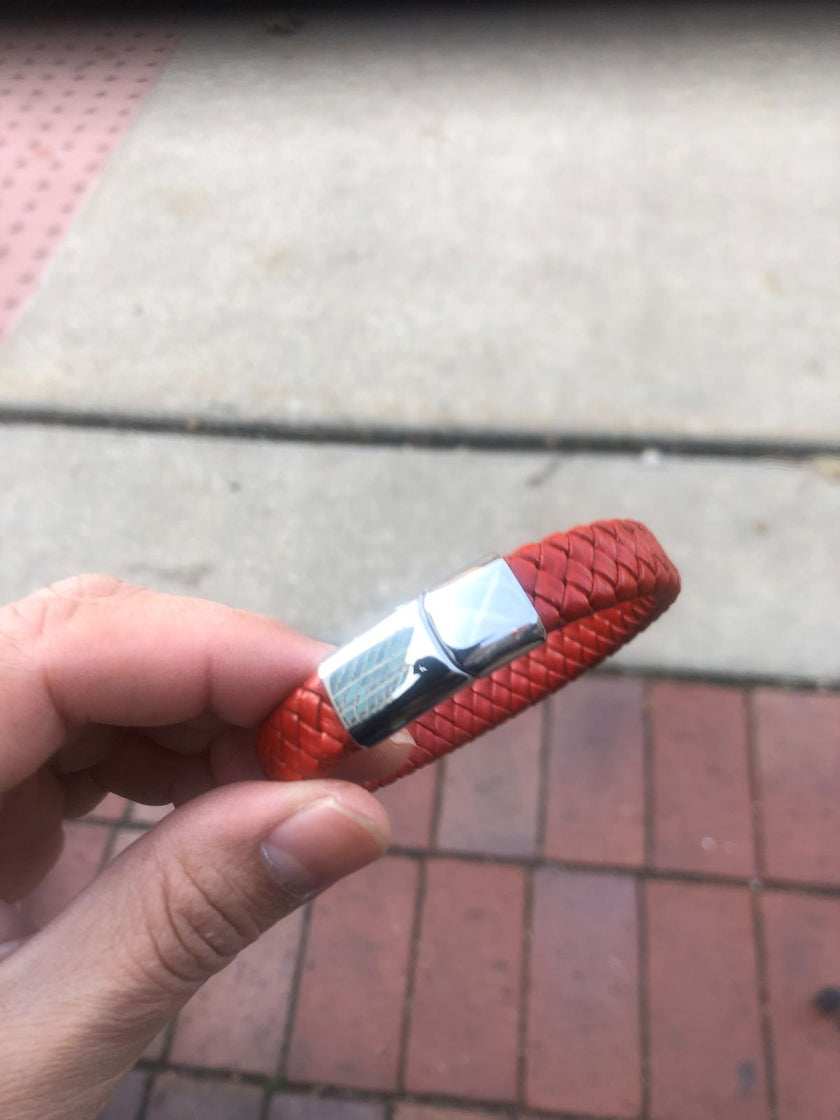Red braided bracelet with a metal clasp held by a hand on a pavement background