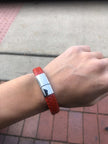 Red bracelet with a silver clasp on a wrist, against a pavement background